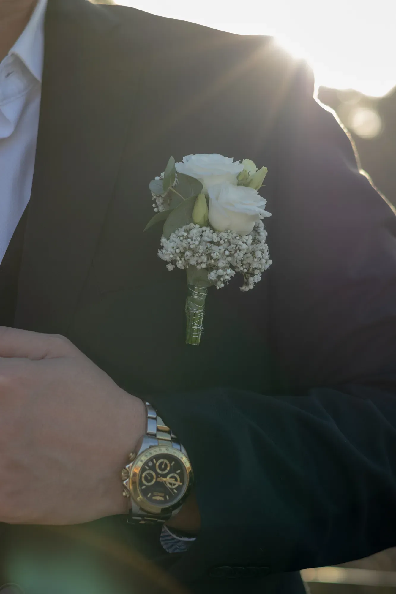 Detail: Anstecker am Hochzeitsanzug und Armbanduhr im Gegenlicht