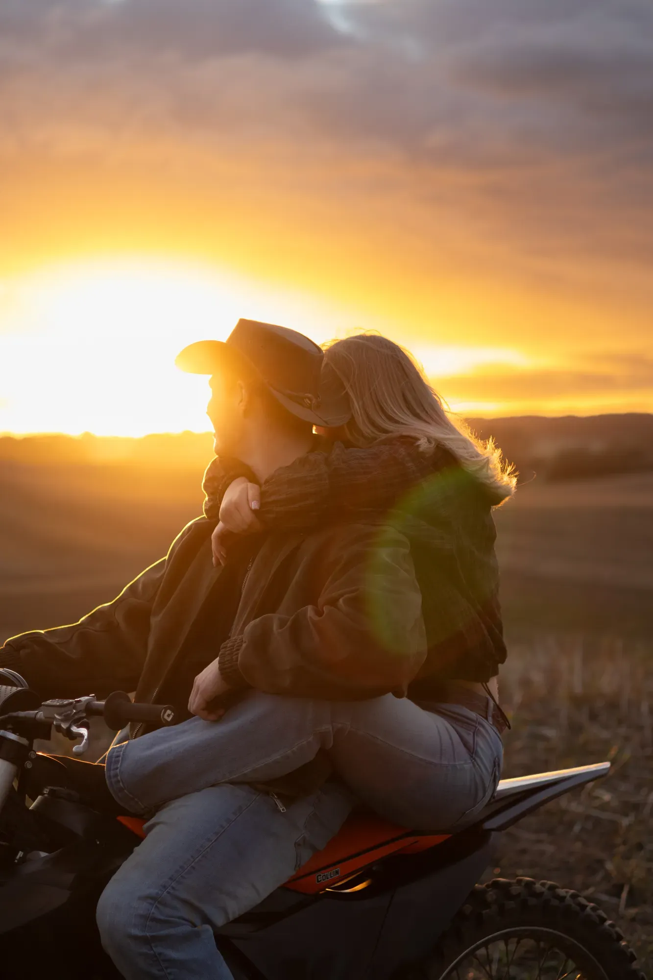 Paar sitzt bei Sonnenuntergang auf einem Motorrad an einem Feld