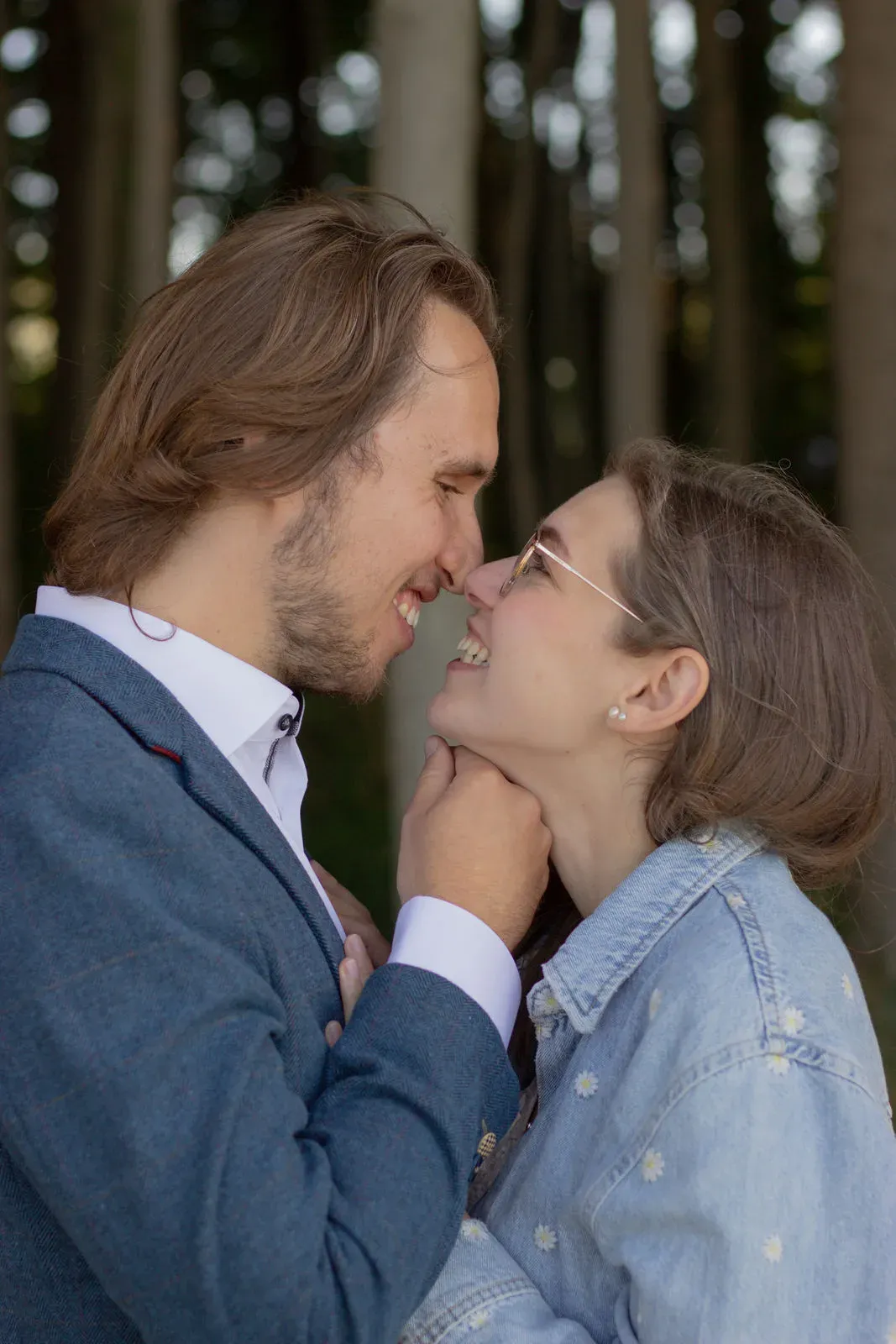 Paar steht Nase an Nase im Wald, er im Blazer, sie in Jeansjacke