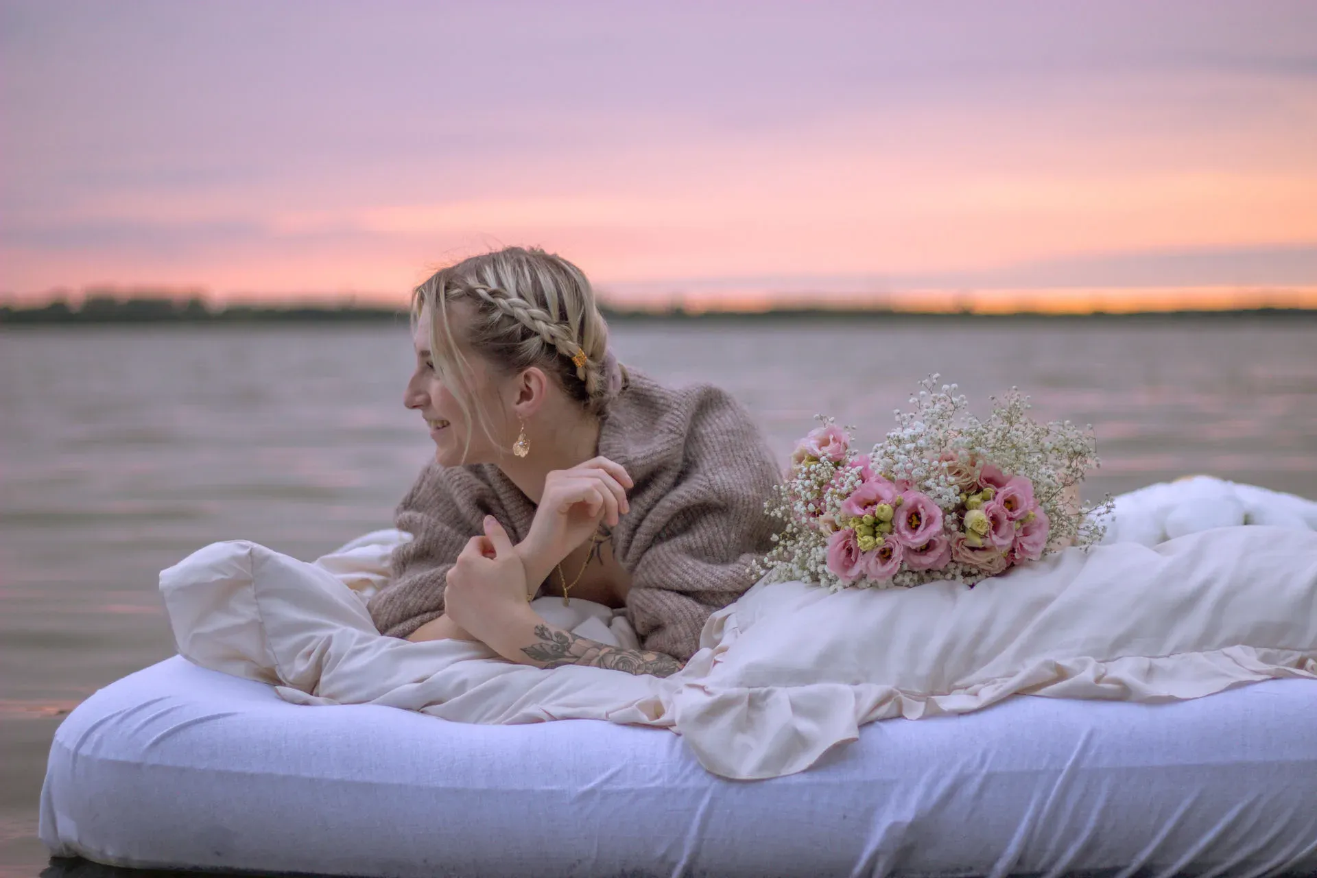 Frau liegt mit Blumenstrauß auf einem Bett am Wasser im Abendrot