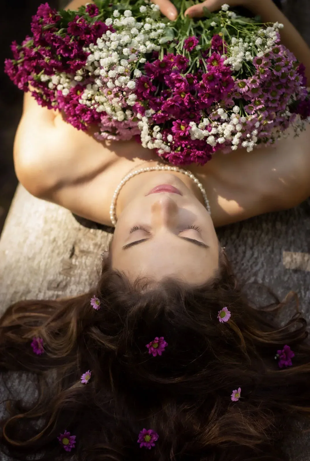 Frau liegt mit geschlossenen Augen unter einem Blumenstrauß, Blüten im Haar