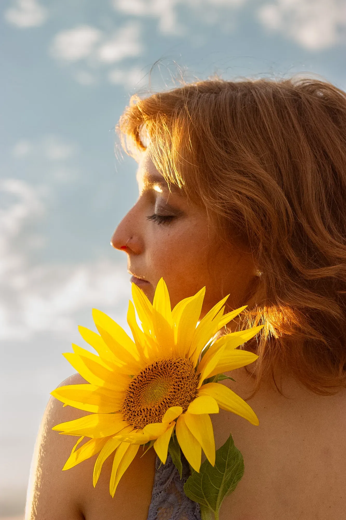Frau im Profil mit geschlossenen Augen, eine Sonnenblume an der Schulter