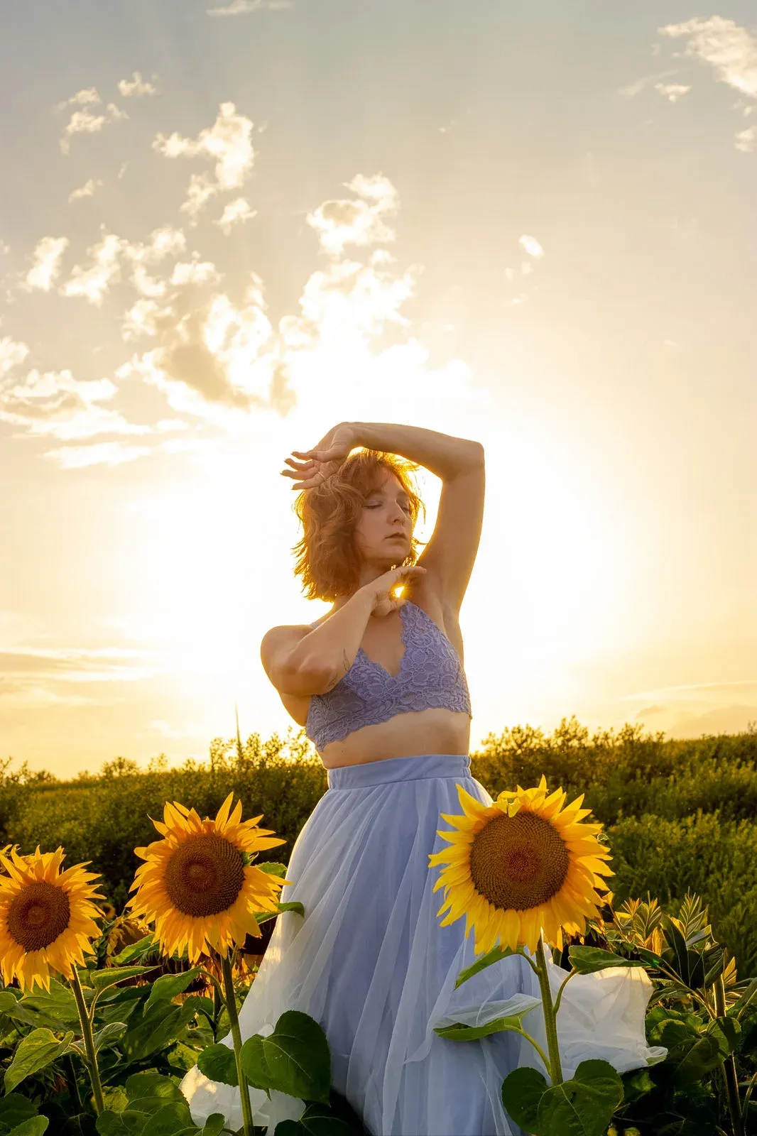 Frau mit erhobenen Armen vor der Sonne zwischen Sonnenblumen