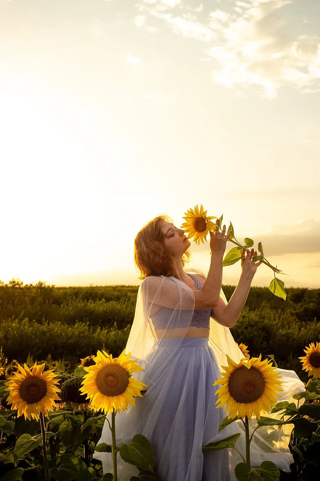 Frau in lilafarbenem Kleid riecht an einer Sonnenblume im Abendlicht