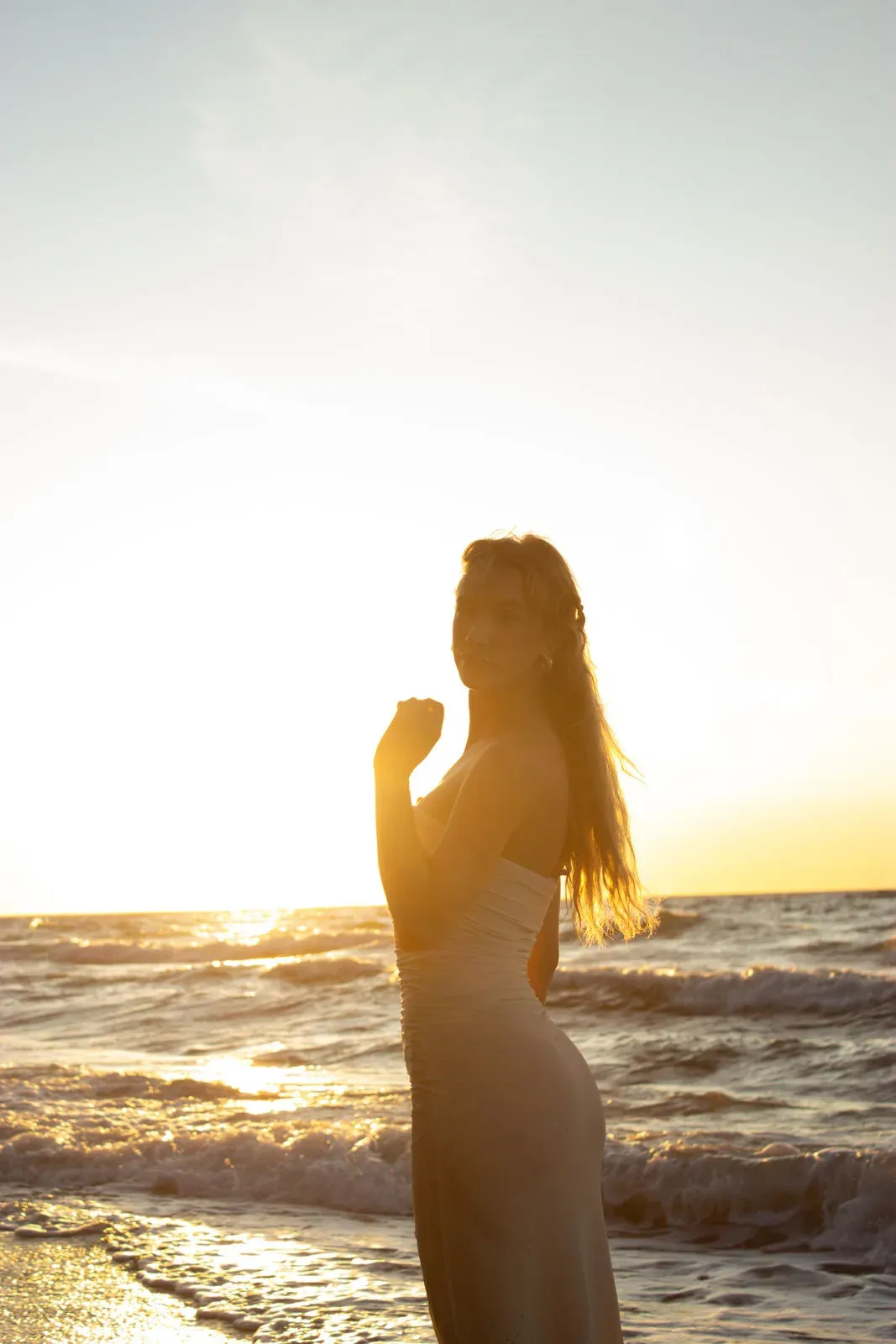 Silhouette einer Frau im langen Kleid vor dem Sonnenuntergang am Meer